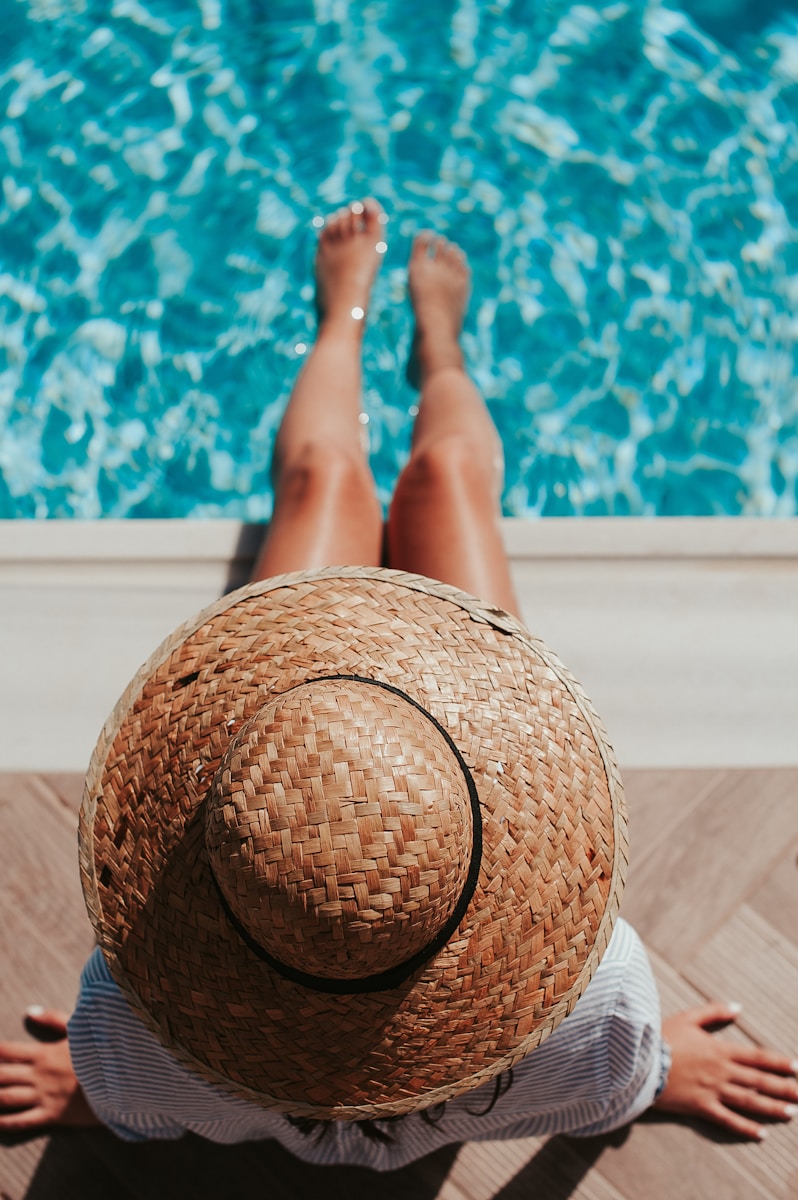 woman sitting on poolside setting both of her feet on pool with summer claims and tips